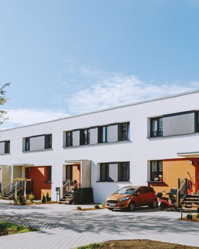 Moderne Reihenhäuser mit farbigen Eingangstüren und gepflastertem Vorplatz an einem sonnigen Tag.
