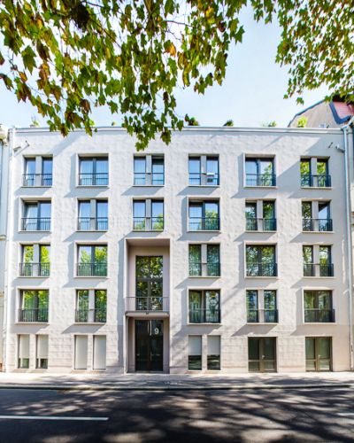 Modernes Stadthaus mit markanter Fassade neben traditionellen Gebäuden, umgeben von Bäumen.