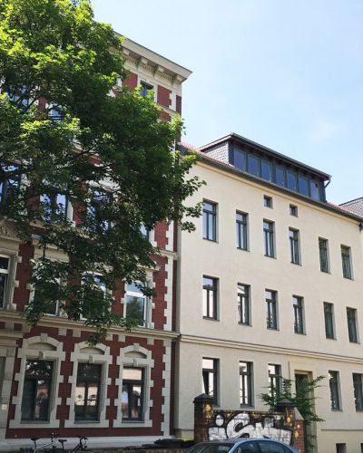 Sanierte Altbauten mit moderner Dachgeschosswohnung, große Fenster, begrünte Umgebung und urbane Wohnlage.