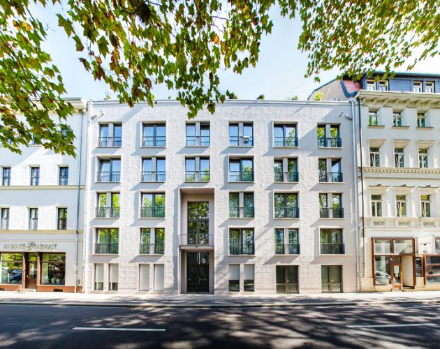 Modernes Stadthaus mit markanter Fassade neben traditionellen Gebäuden, umgeben von Bäumen.