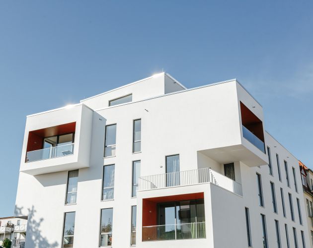Modernes Wohngebäude mit weißen Fassaden und roten Akzenten unter klarem Himmel.