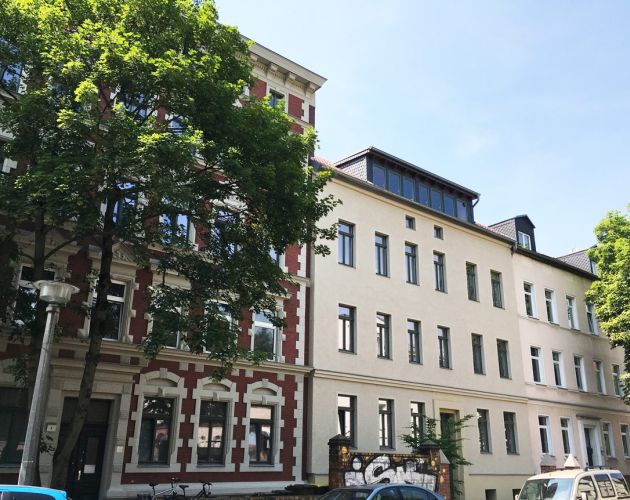 Sanierte Altbauten mit moderner Dachgeschosswohnung, große Fenster, begrünte Umgebung und urbane Wohnlage.